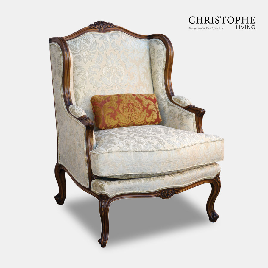 Timber wingback armchair with upholstered armrests and a carved motif at top and a red cushion to add richness.