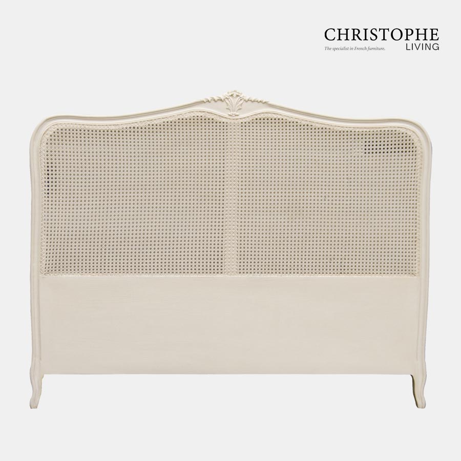 A painted French style bedhead upholstered with cane and finished in antique white with carving details