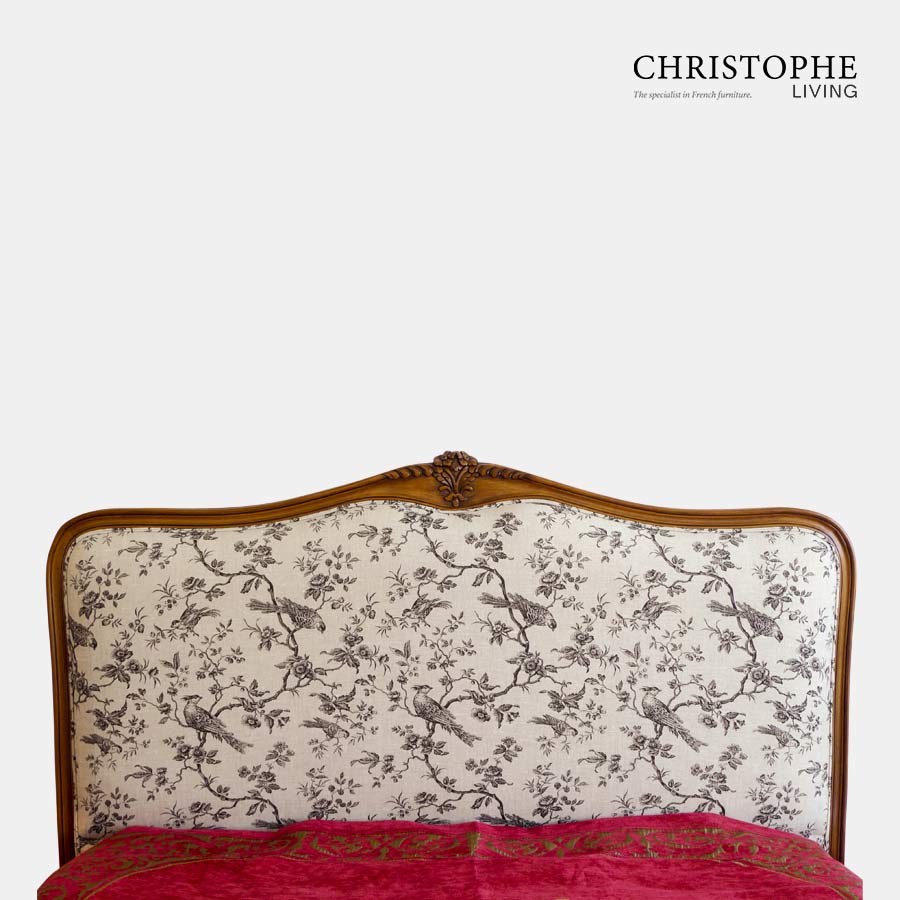 A French provincial bedhead upholstered in grey and cream bird toile linen fabric with timber in walnut finish